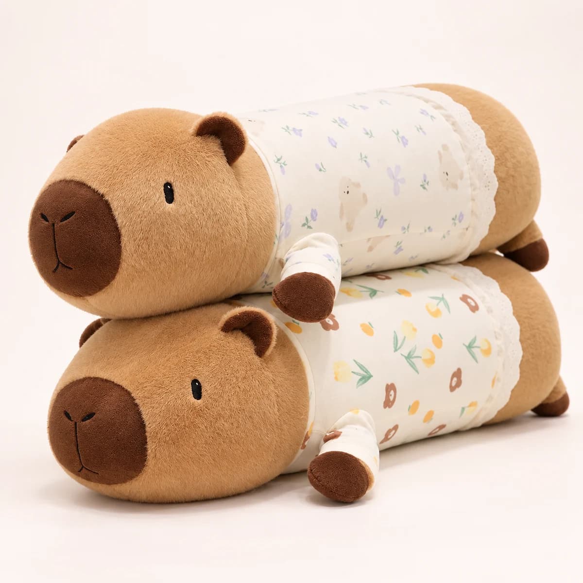 Two long capybara plush toys in cream pajamas with lilac and yellow floral prints Two long capybara plush toys in cream pajamas with lilac and yellow floral prints