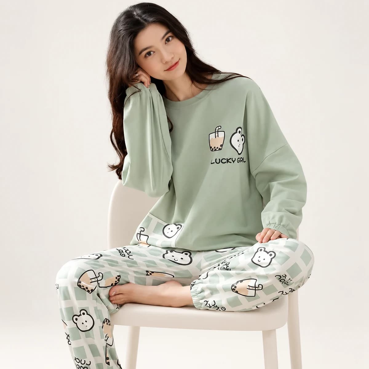 Sage green boba pajama set with cartoon animal motifs and checked trousers, shown on a seated adult model Sage green boba pajama set with cartoon animal motifs and checked trousers, shown on a seated adult model