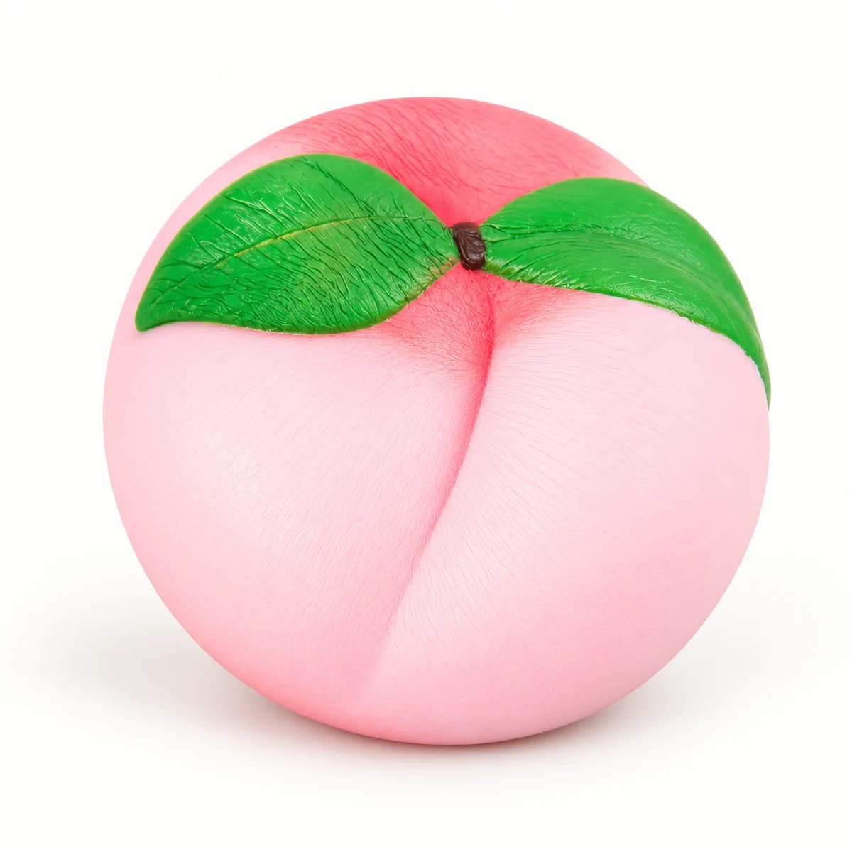 Pink peach-shaped squishy with two green leaves on a warm white studio surface Pink peach-shaped squishy with two green leaves on a warm white studio surface